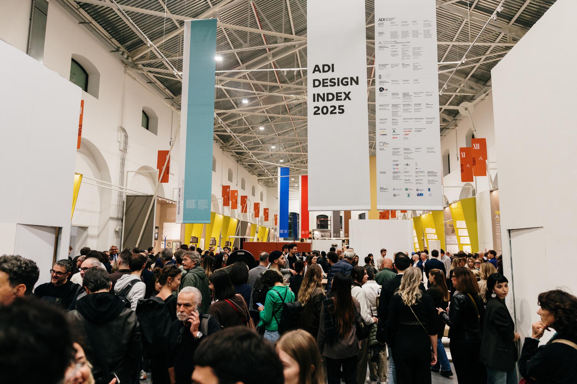 Folla di persone a un evento design con banner ADI Design Index 2025 in un ampio spazio espositivo illuminato.
