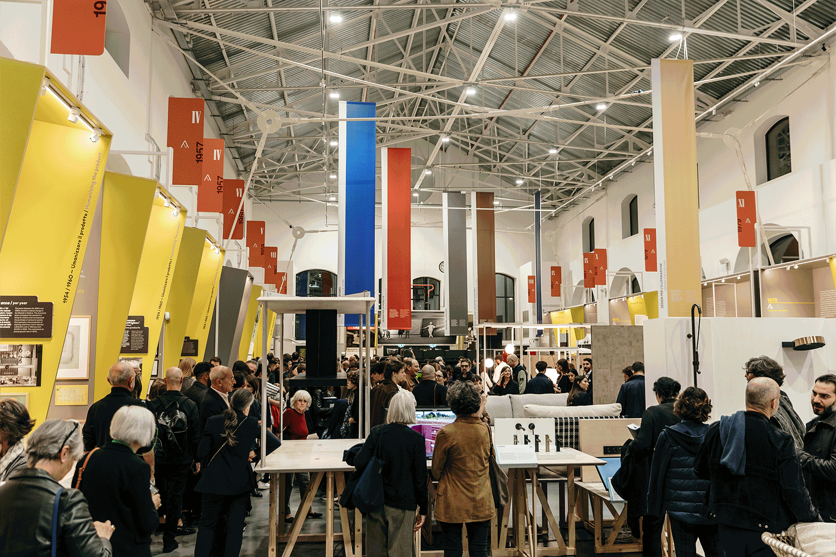 Persone visitano una mostra in un ampio spazio con pannelli colorati e schede informative appese.
