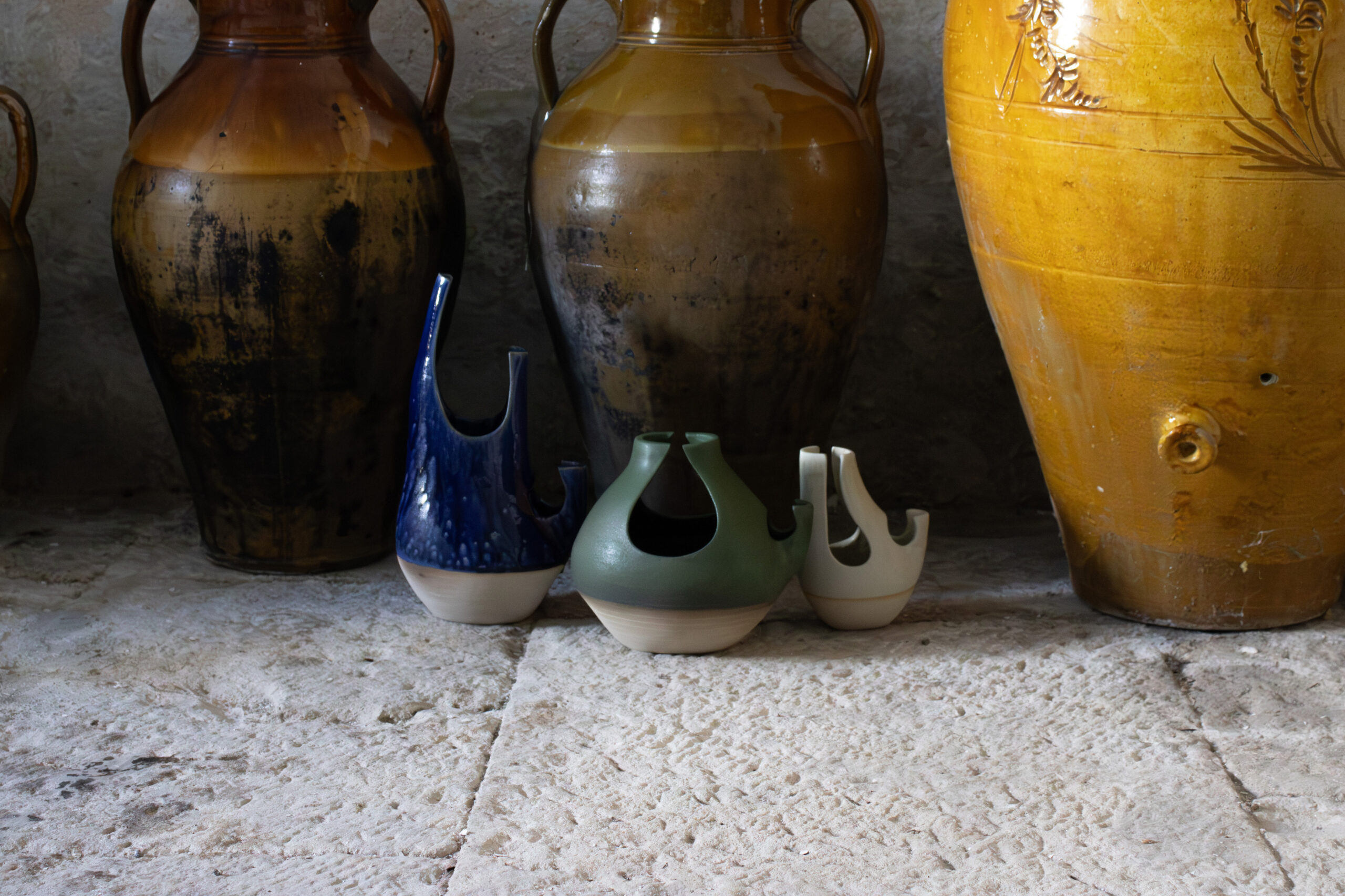 Vasi di ceramica colorati su pavimento di pietra, con anfore artigianali sullo sfondo.