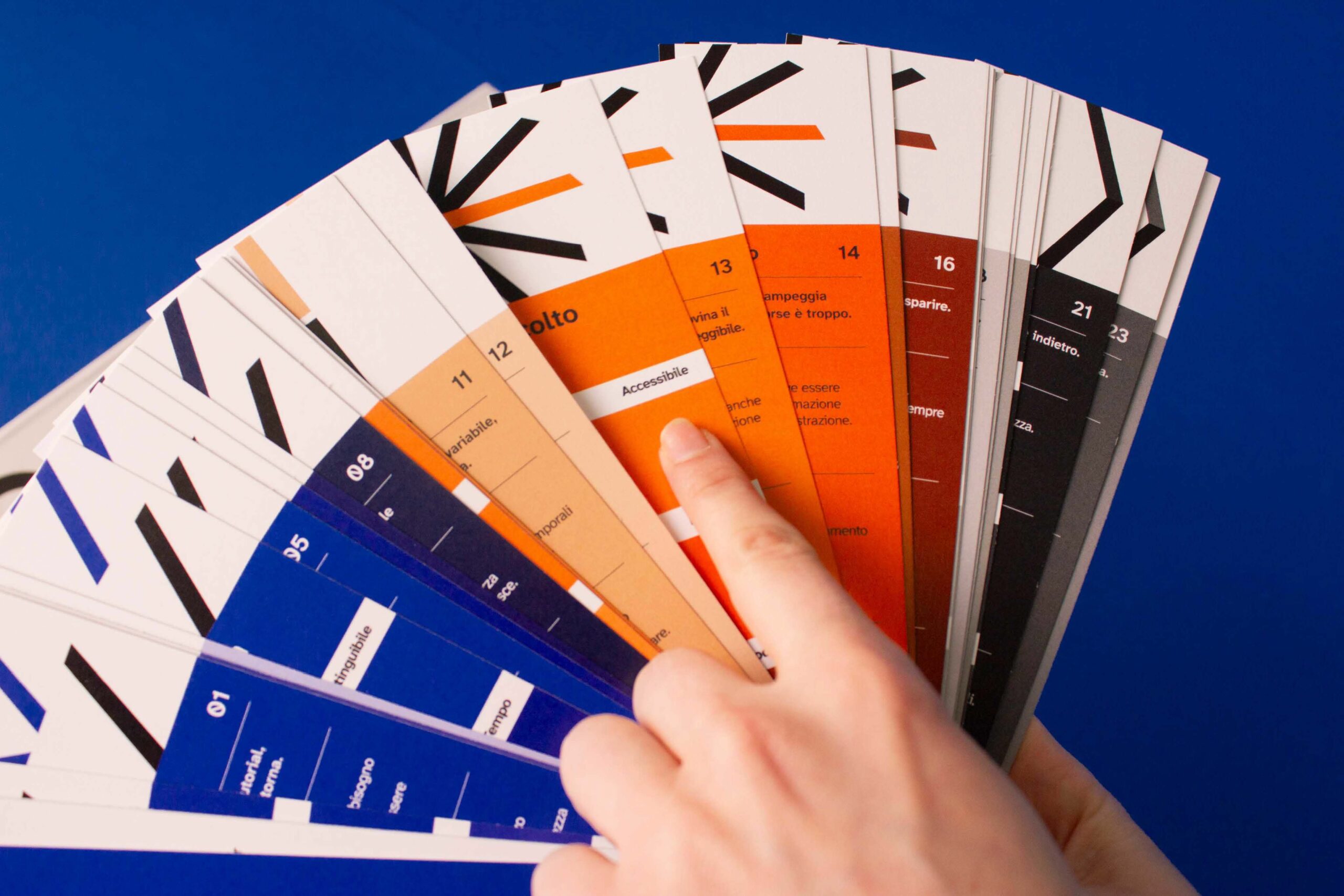 Dita sfogliano un ventaglio di schede colorate con testo su sfondo blu, focalizzando su una scheda arancione.