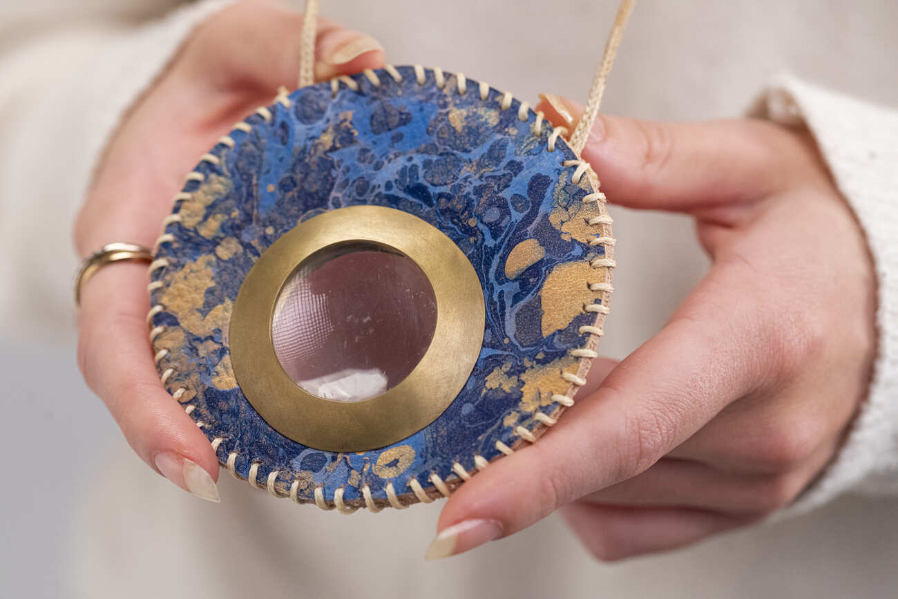 Collana artigianale con pendente blu e dorato, tenuta in mano per esibire il suo design unico e dettagliato.