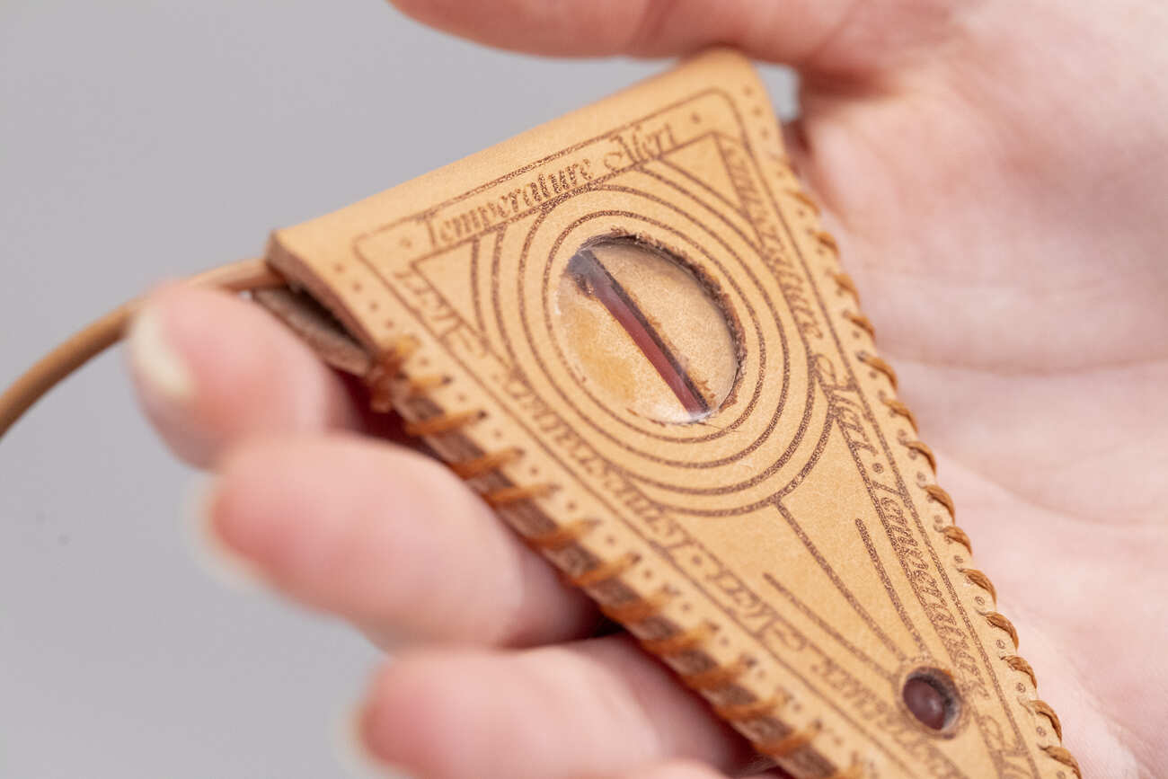 Mano tiene strumento antico in legno con incisioni, probabilmente un rudimentale dispositivo di misurazione.