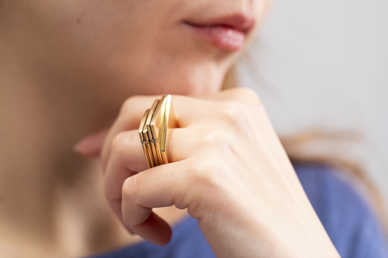 Persona con anelli dorati moderni sulla mano, riflette in una posa pensierosa.