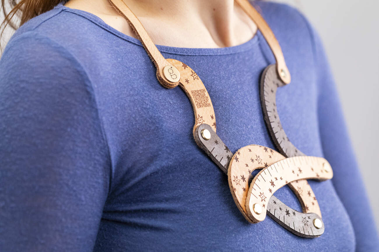 Collana artigianale in legno con dettagli incisi, indossata su maglia blu a maniche lunghe.