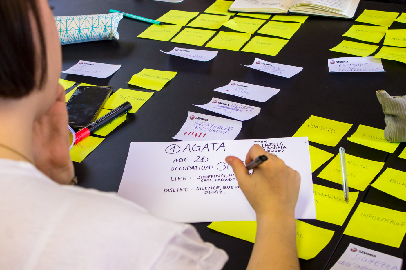 Persona scrive su foglio tra post-it gialli su un tavolo, attività creativa di brainstorming.