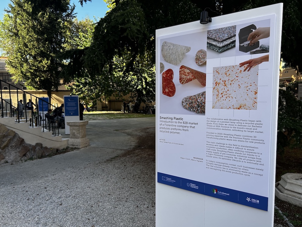 Tabellone informativo su progetti di design sostenibile con polimeri riciclati, esposto in un ambiente esterno.