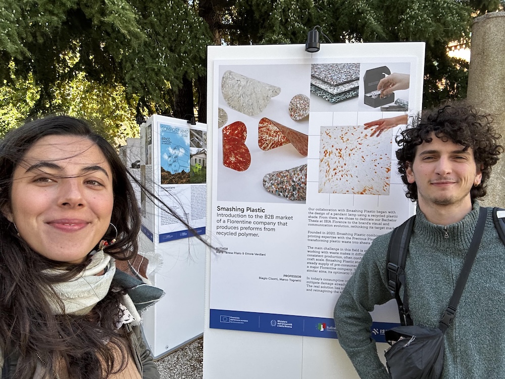 Due persone sorridenti davanti a un poster su soluzioni innovative per il riciclo della plastica.