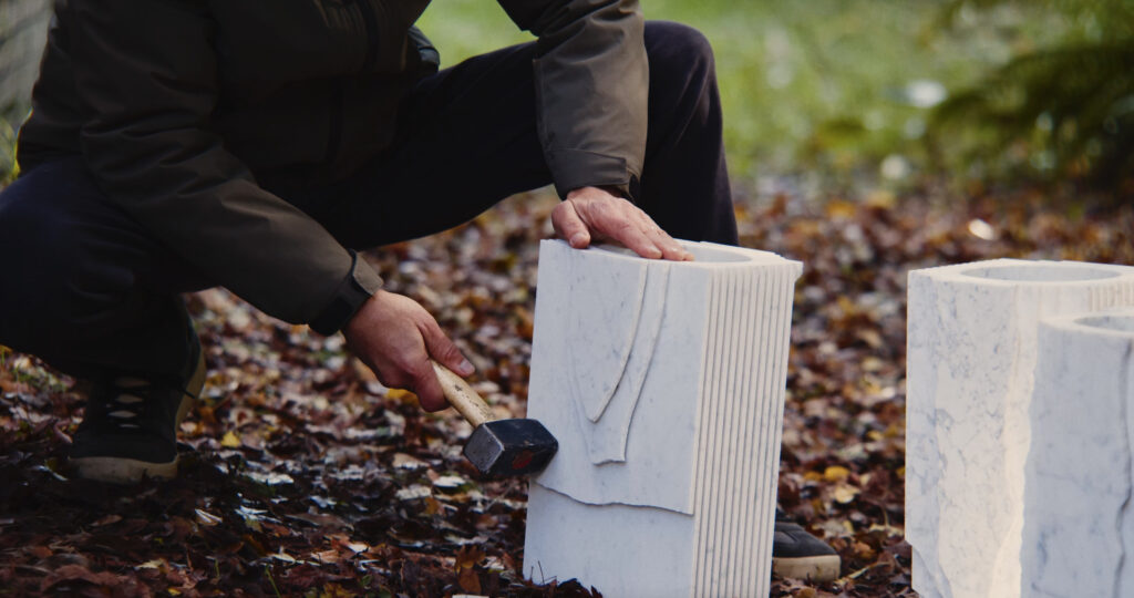 Scultore mentre lavora su un blocco di marmo in un ambiente autunnale con foglie cadute.
