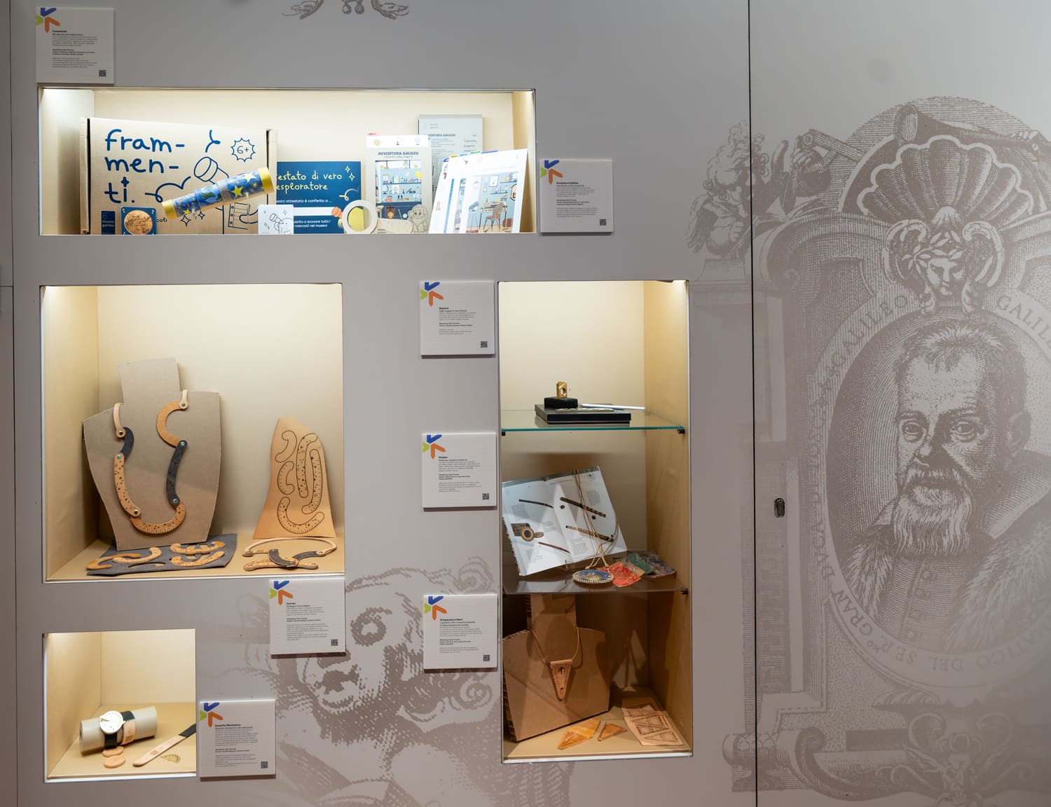 Esposizione di strumenti scientifici e design in vetrina museale, con accenni a Galileo e illustrazioni murali.