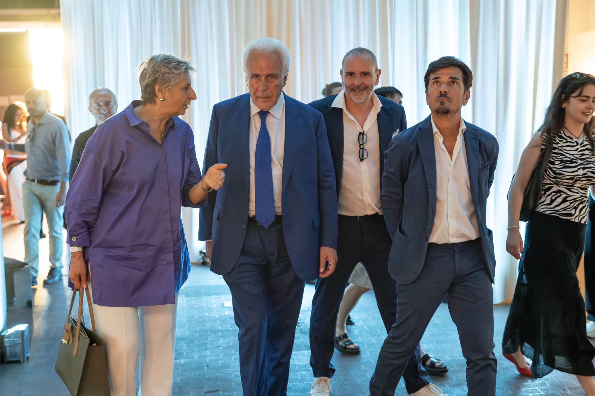Gruppo di persone vestite elegantemente cammina in un ambiente interno ben illuminato.