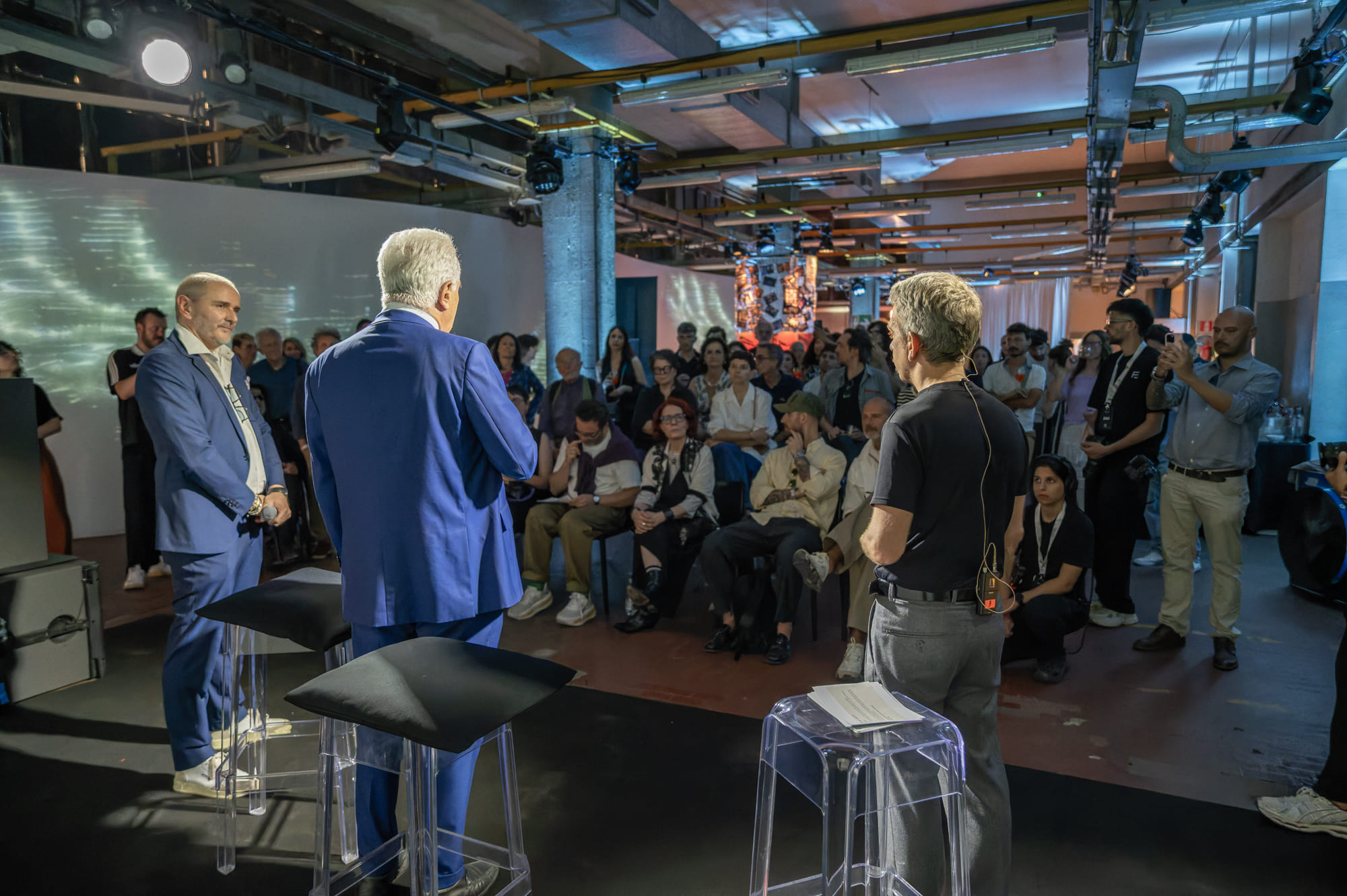 Relatori parlano a una folla attenta durante un evento in un ambiente industriale moderno.