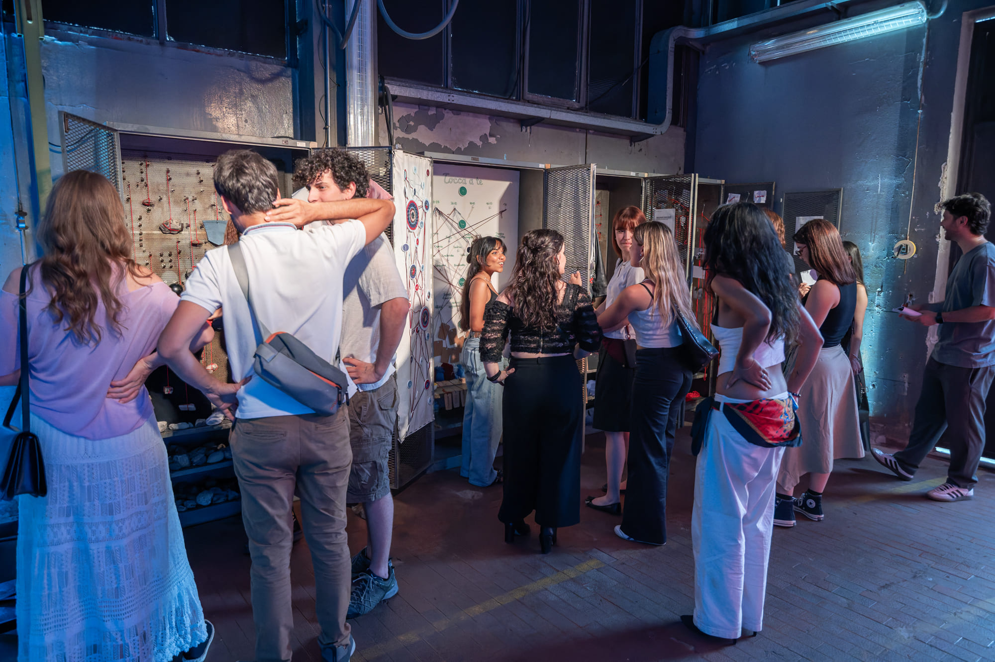 Gruppo di persone conversa e osserva opere d'arte in un evento espositivo, immersi in un'atmosfera luminosa e vivace.