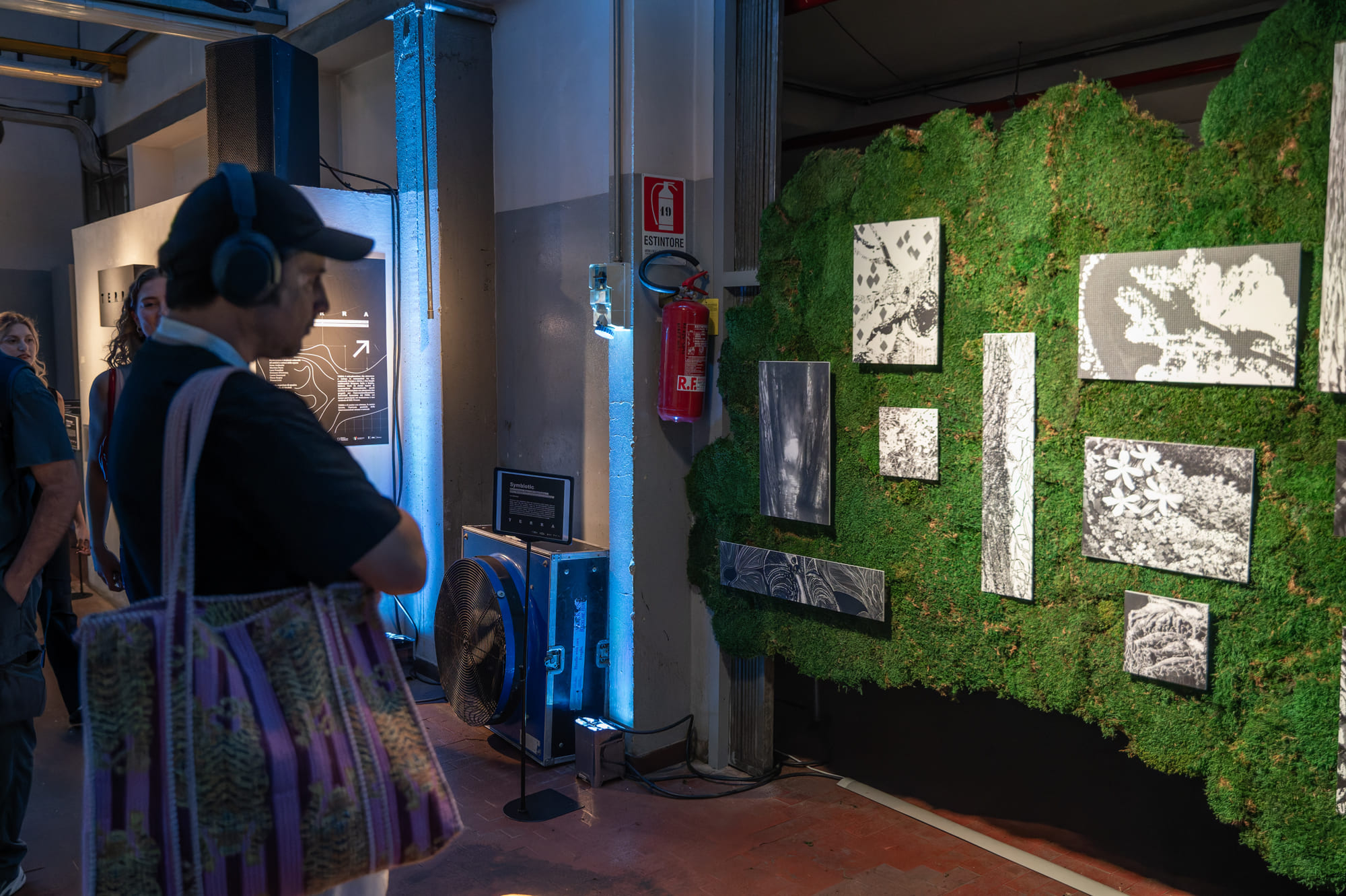 Mostra d'arte con visitatori che ammirano fotografie in bianco e nero su parete verde decorativa.