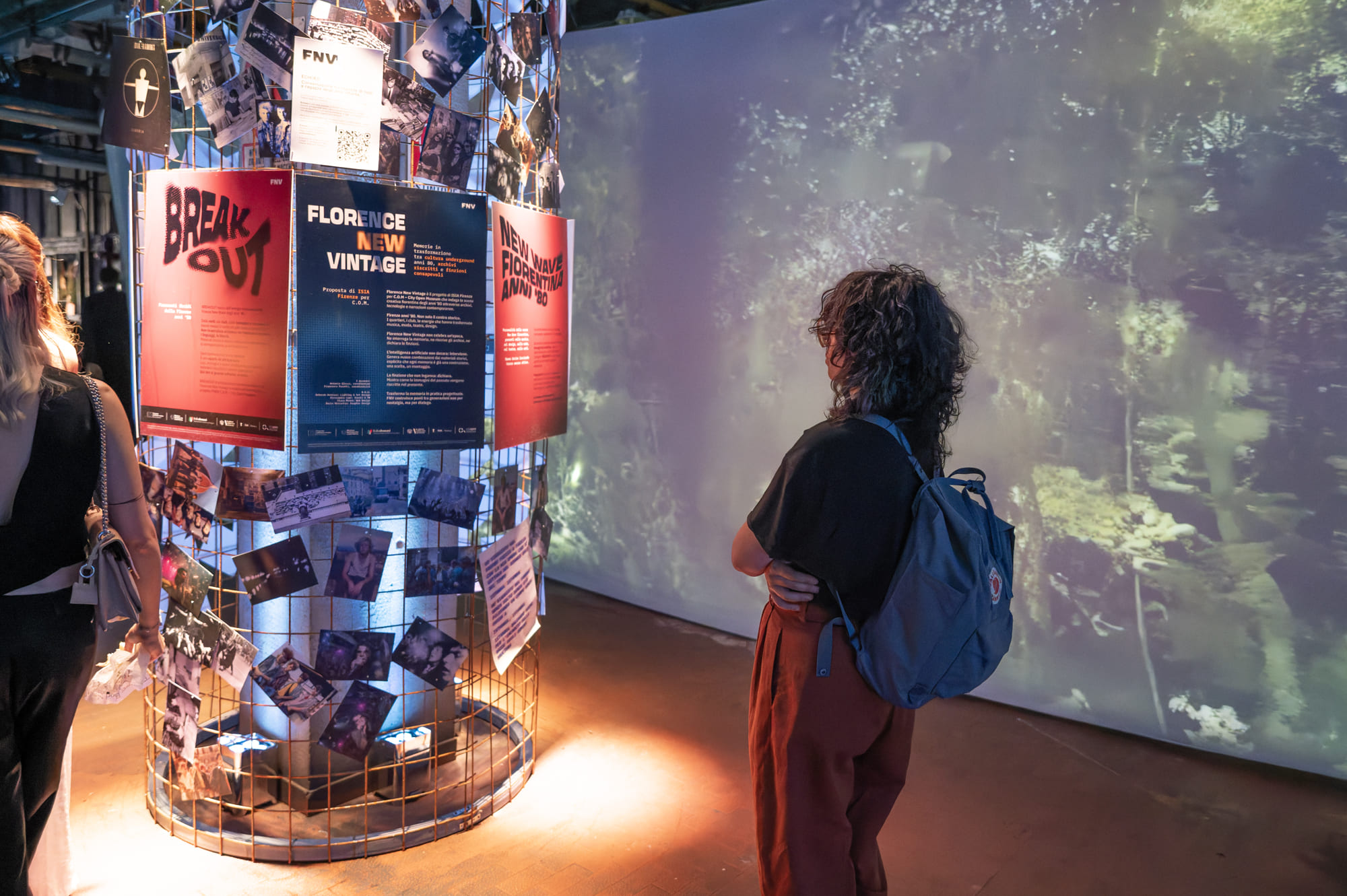 Persona osserva un'installazione di manifesti e foto in un ambiente futuristico e artistico con illuminazione creativa.