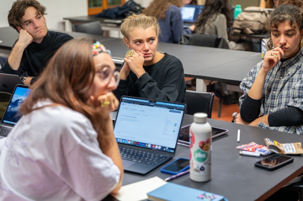 Persone in aula che discutono attorno a un tavolo con laptop aperti, pensierosi e concentrati.
