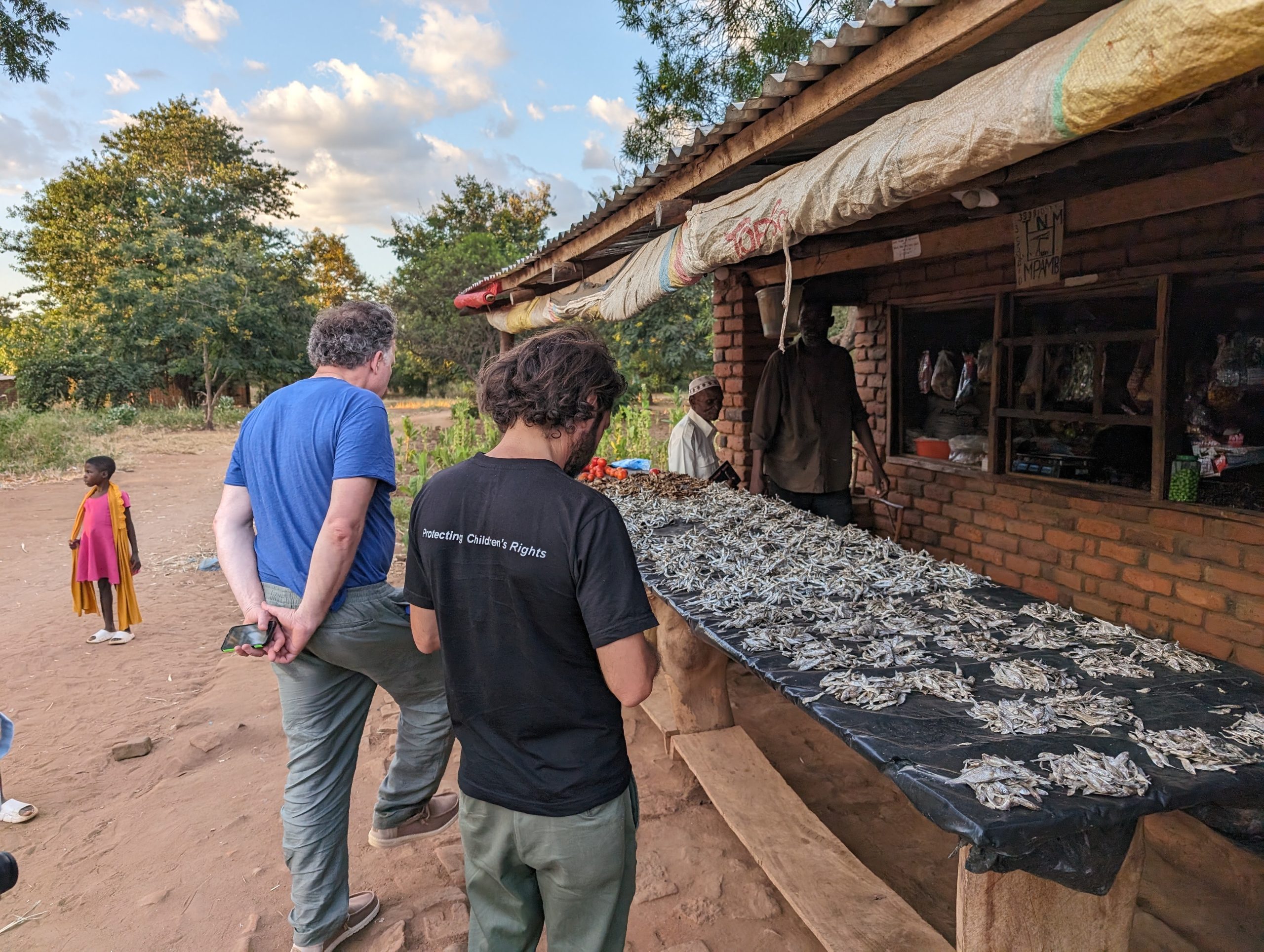 Due persone esaminano il pesce essiccato esposto su banchi all'aperto in un mercato locale.