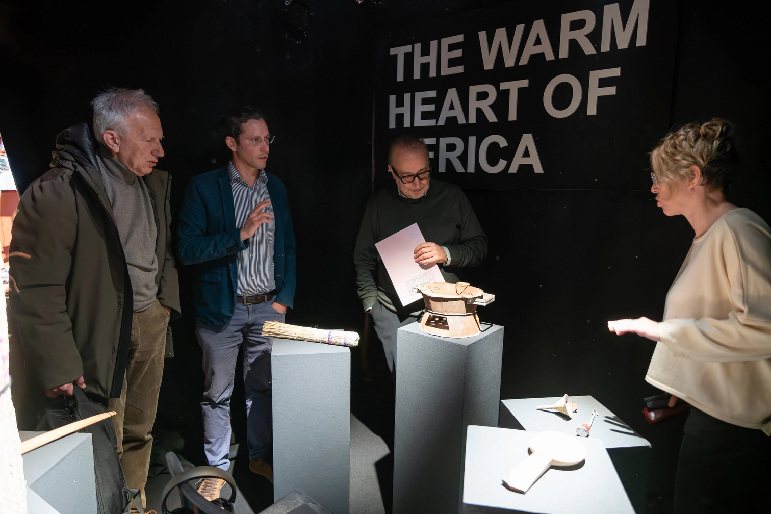 Persone osservano una mostra dal tema The Warm Heart of Africa con oggetti esposti su piedistalli.