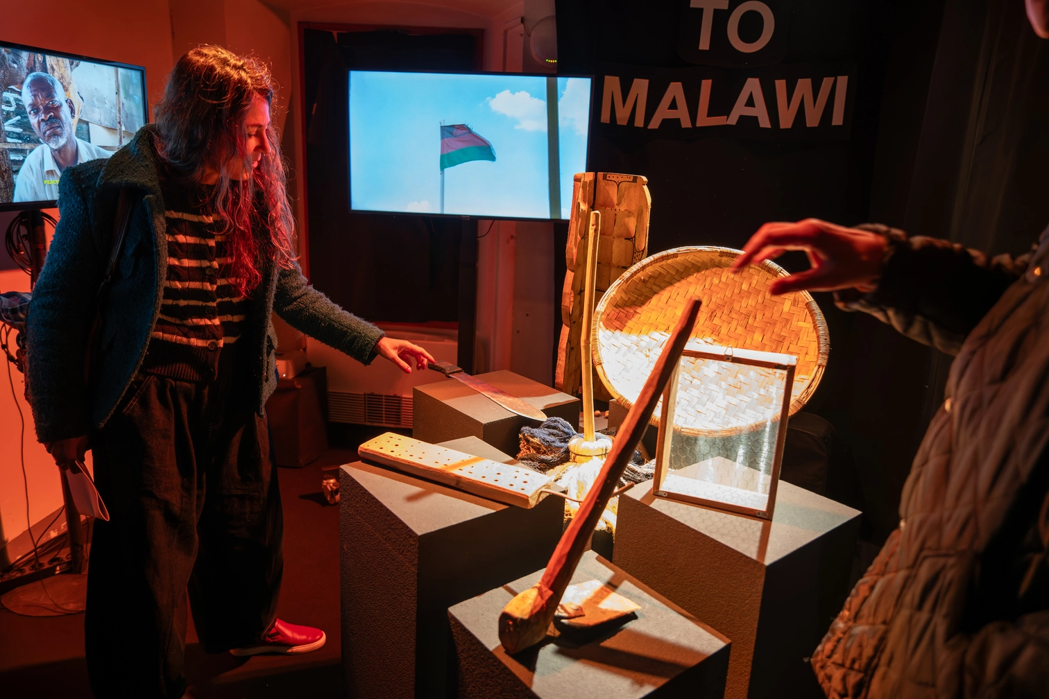 Donna esamina esposizione culturale con strumenti tradizionali africani e video di bandiera del Malawi.